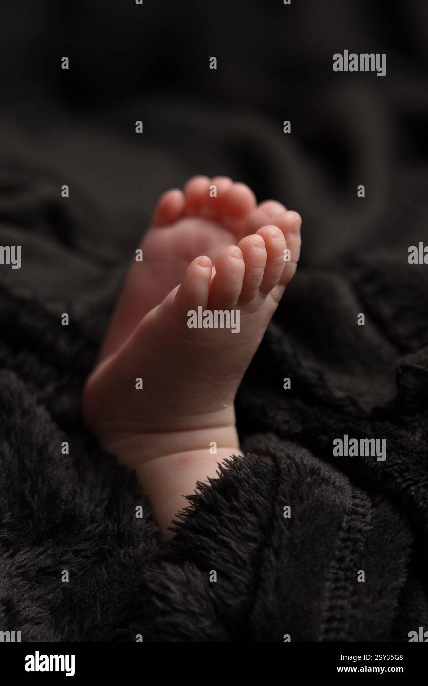 Pieds de bébé isolés sur un fond de tissu noir, en se concentrant sur le pied le plus proche. Image créative des détails du nouveau-né. Banque D'Images