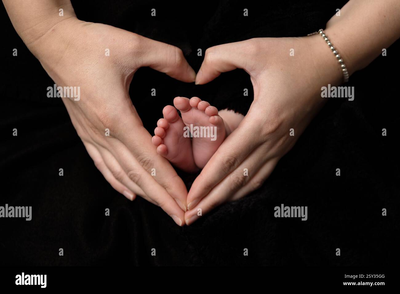 Les mains des parents dans une forme de coeur entourant une paire de petits pieds de bébé, représentant l'amour que les parents ont pour leur nouveau-né. Banque D'Images