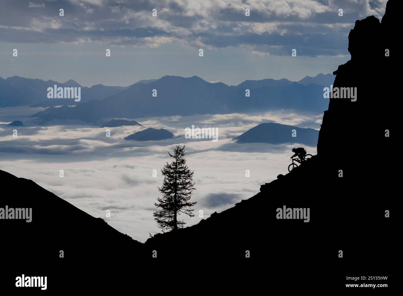 Un homme monte un VTT au-dessus d'une inversion de nuages sur la colle della Fauniera, un col de montagne dans les Alpes Cottiennes, Piémont, dans le nord de l'Italie. Banque D'Images