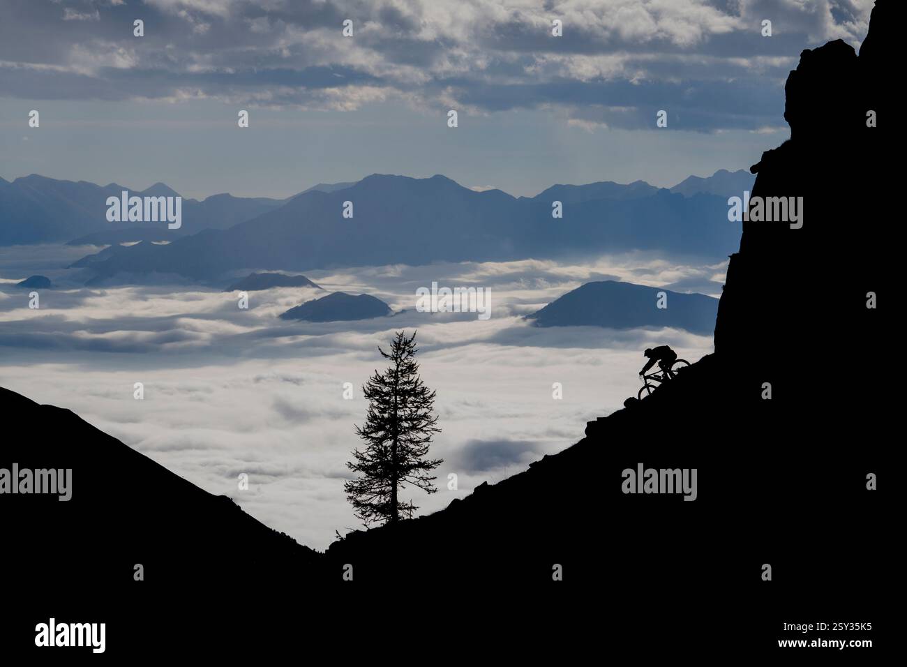 Un homme monte un VTT au-dessus d'une inversion de nuages sur la colle della Fauniera, un col de montagne dans les Alpes Cottiennes, Piémont, dans le nord de l'Italie. Banque D'Images