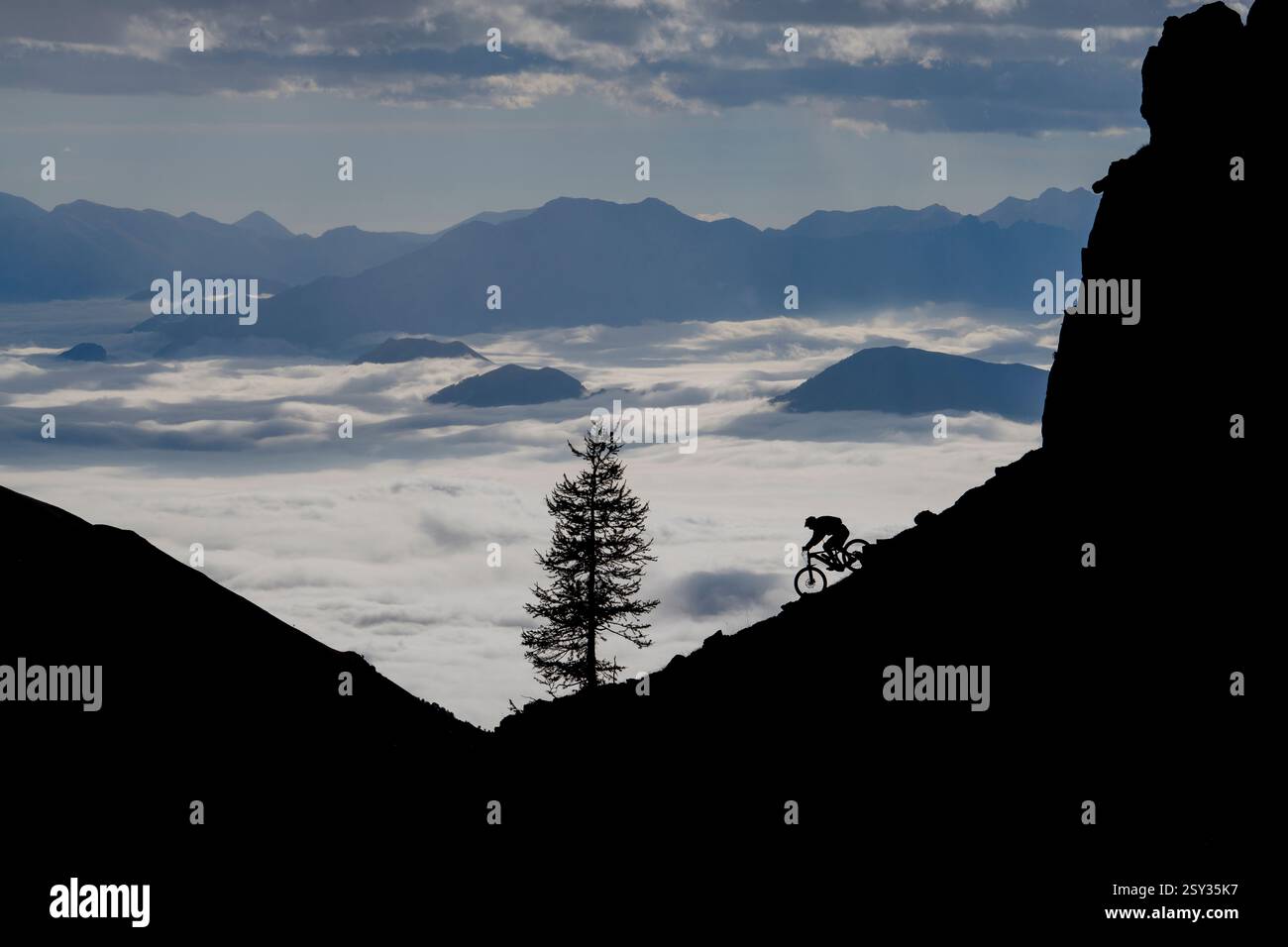 Un homme monte un VTT au-dessus d'une inversion de nuages sur la colle della Fauniera, un col de montagne dans les Alpes Cottiennes, Piémont, dans le nord de l'Italie. Banque D'Images