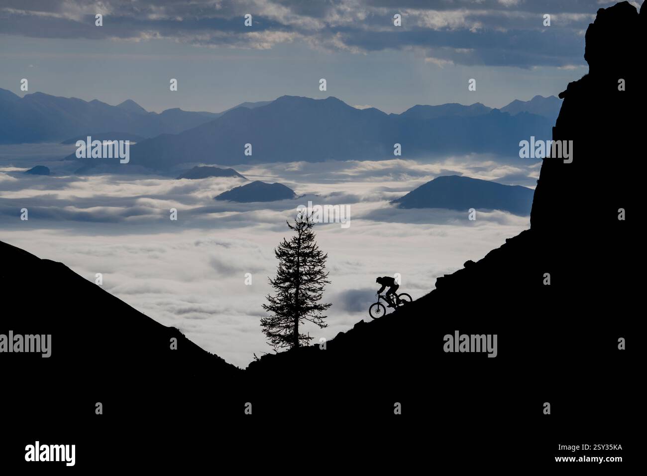 Un homme monte un VTT au-dessus d'une inversion de nuages sur la colle della Fauniera, un col de montagne dans les Alpes Cottiennes, Piémont, dans le nord de l'Italie. Banque D'Images