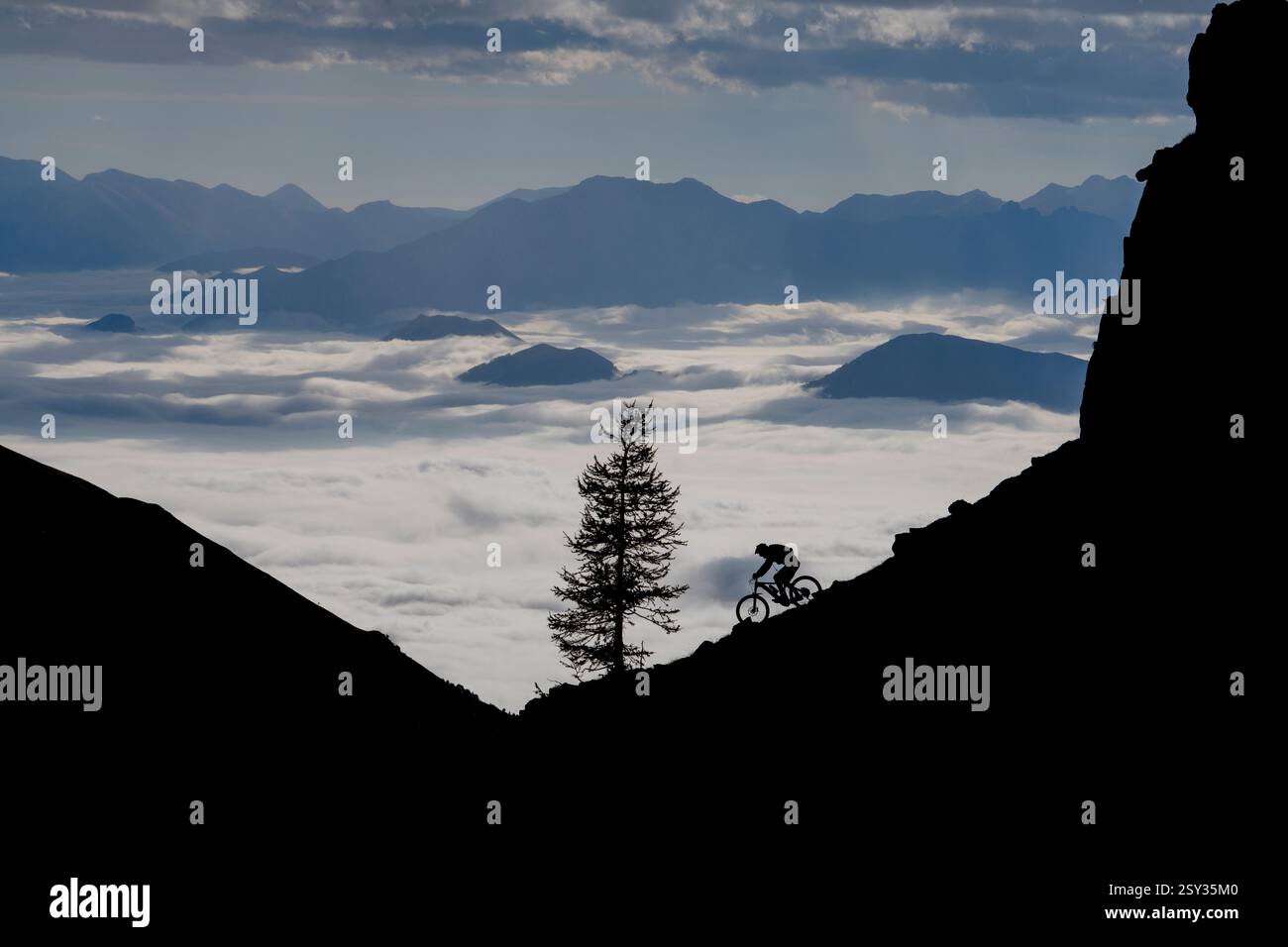Un homme monte un VTT au-dessus d'une inversion de nuages sur la colle della Fauniera, un col de montagne dans les Alpes Cottiennes, Piémont, dans le nord de l'Italie. Banque D'Images
