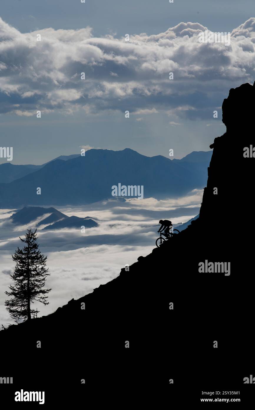 Un homme monte un VTT au-dessus d'une inversion de nuages sur la colle della Fauniera, un col de montagne dans les Alpes Cottiennes, Piémont, dans le nord de l'Italie. Banque D'Images