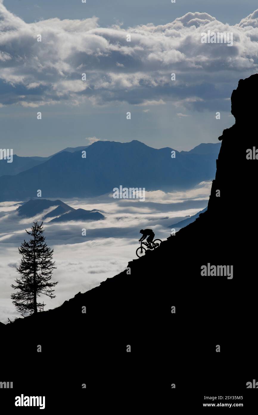 Un homme monte un VTT au-dessus d'une inversion de nuages sur la colle della Fauniera, un col de montagne dans les Alpes Cottiennes, Piémont, dans le nord de l'Italie. Banque D'Images