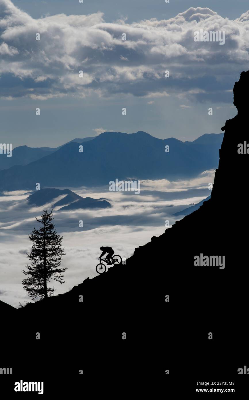 Un homme monte un VTT au-dessus d'une inversion de nuages sur la colle della Fauniera, un col de montagne dans les Alpes Cottiennes, Piémont, dans le nord de l'Italie. Banque D'Images