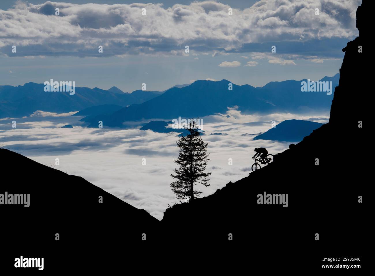 Un homme monte un VTT au-dessus d'une inversion de nuages sur la colle della Fauniera, un col de montagne dans les Alpes Cottiennes, Piémont, dans le nord de l'Italie. Banque D'Images