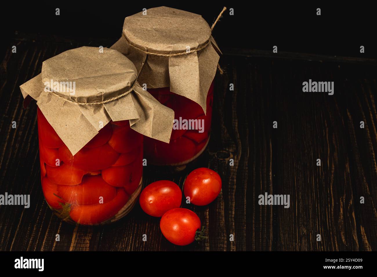 Deux pots remplis de tomates marinées et de concombres sont assis sur une table en bois sombre, mettant en valeur les couleurs vibrantes des légumes conservés, prêts pour e. Banque D'Images