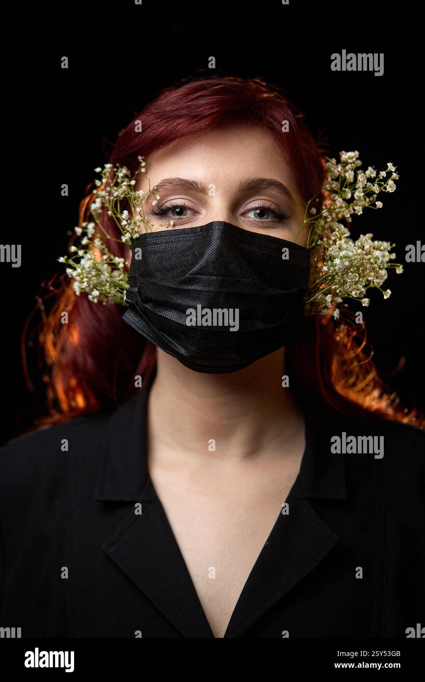 Femme aux cheveux rouges portant un masque noir orné de fleurs délicates en portrait présentant un concept de style unique Banque D'Images