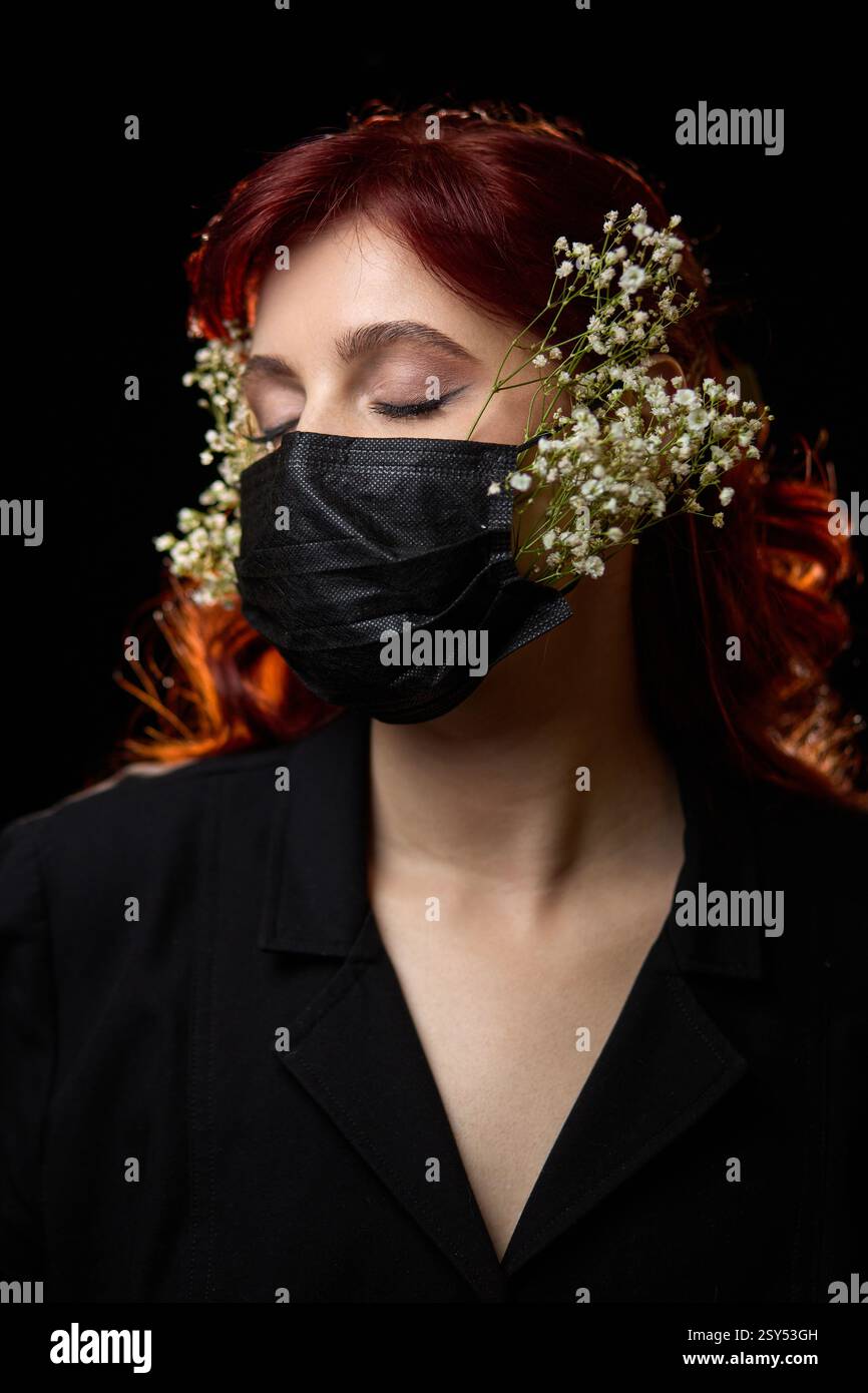 Portrait d'une femme portant un masque noir orné de fleurs blanches dans ses cheveux roux, un concept artistique avec des éléments floraux Banque D'Images