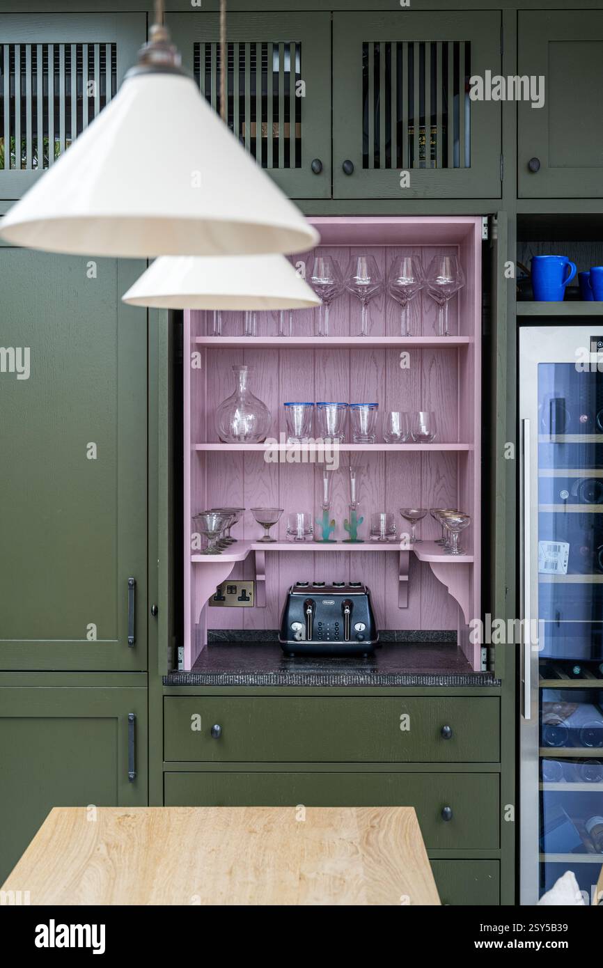 Verrerie sur étagères roses dans une cuisine vert olive contrastée dans la refonte contemporaine de la maison West London. Banque D'Images