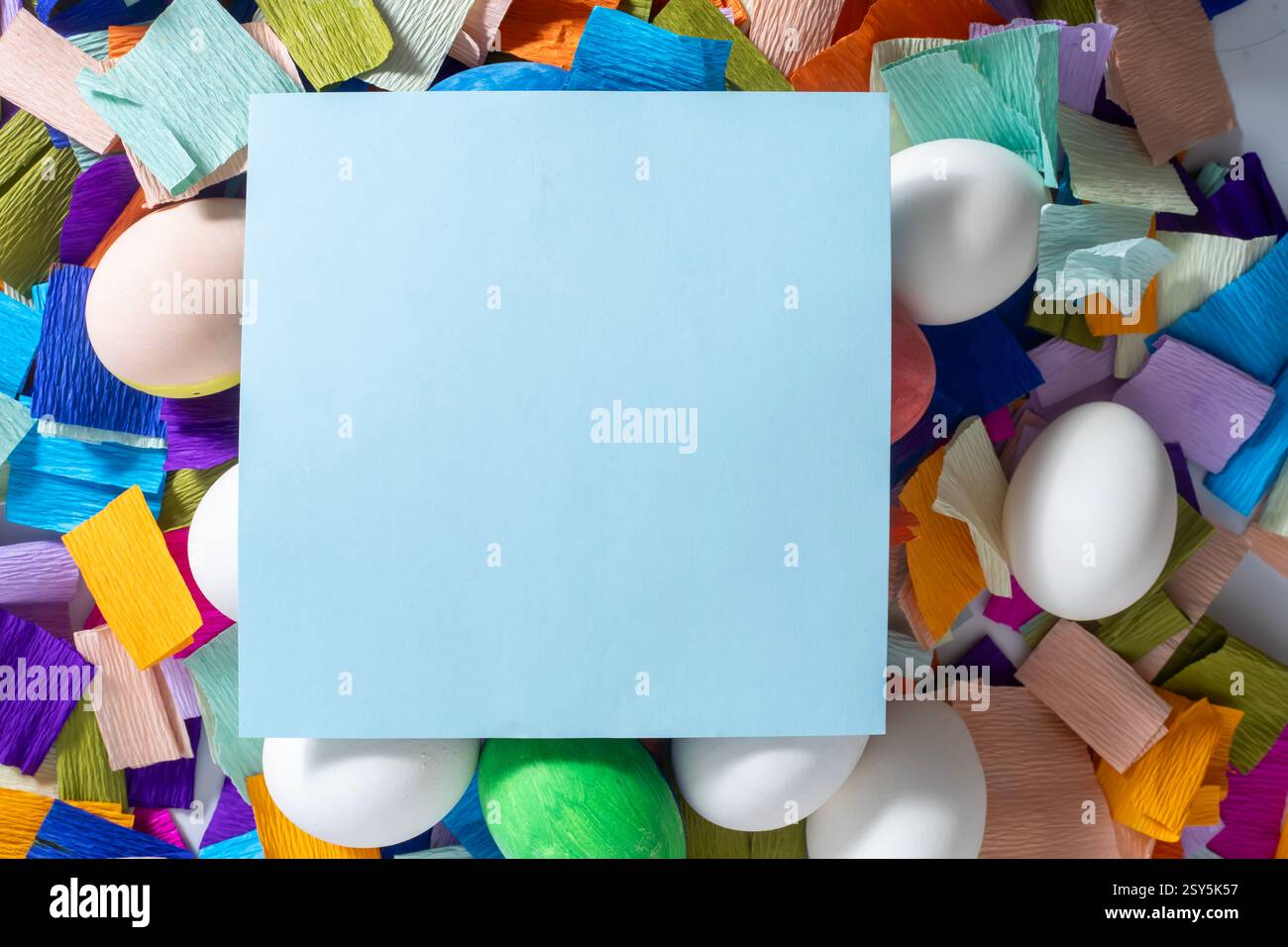 Un carnet jaune vierge entouré d'œufs colorés et de morceaux de papier vibrants pour la célébration de Pâques. Banque D'Images