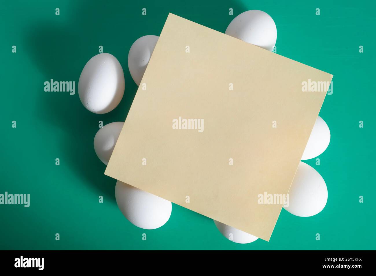 Joyeuses Pâques. Une feuille de papier vierge placée sur le dessus d'un œuf blanc placé sur un fond vert vif. Banque D'Images
