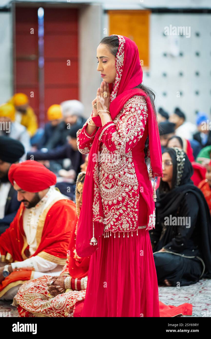 Une jolie femme sikhe vêtue de beaux vêtements rouges médite à l'autel du temple avec ses mains serrées. À New York. Banque D'Images