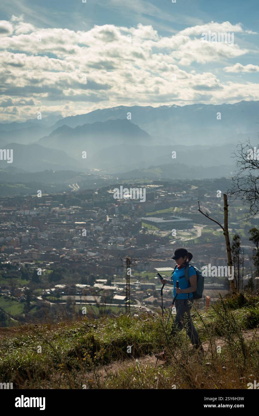 Une femme avec des bâtons de randonnée marche le long du sommet de la montagne Naranco à Oviedo, en Espagne avec un arrière-plan fabuleux de la ville et du ciel. Banque D'Images