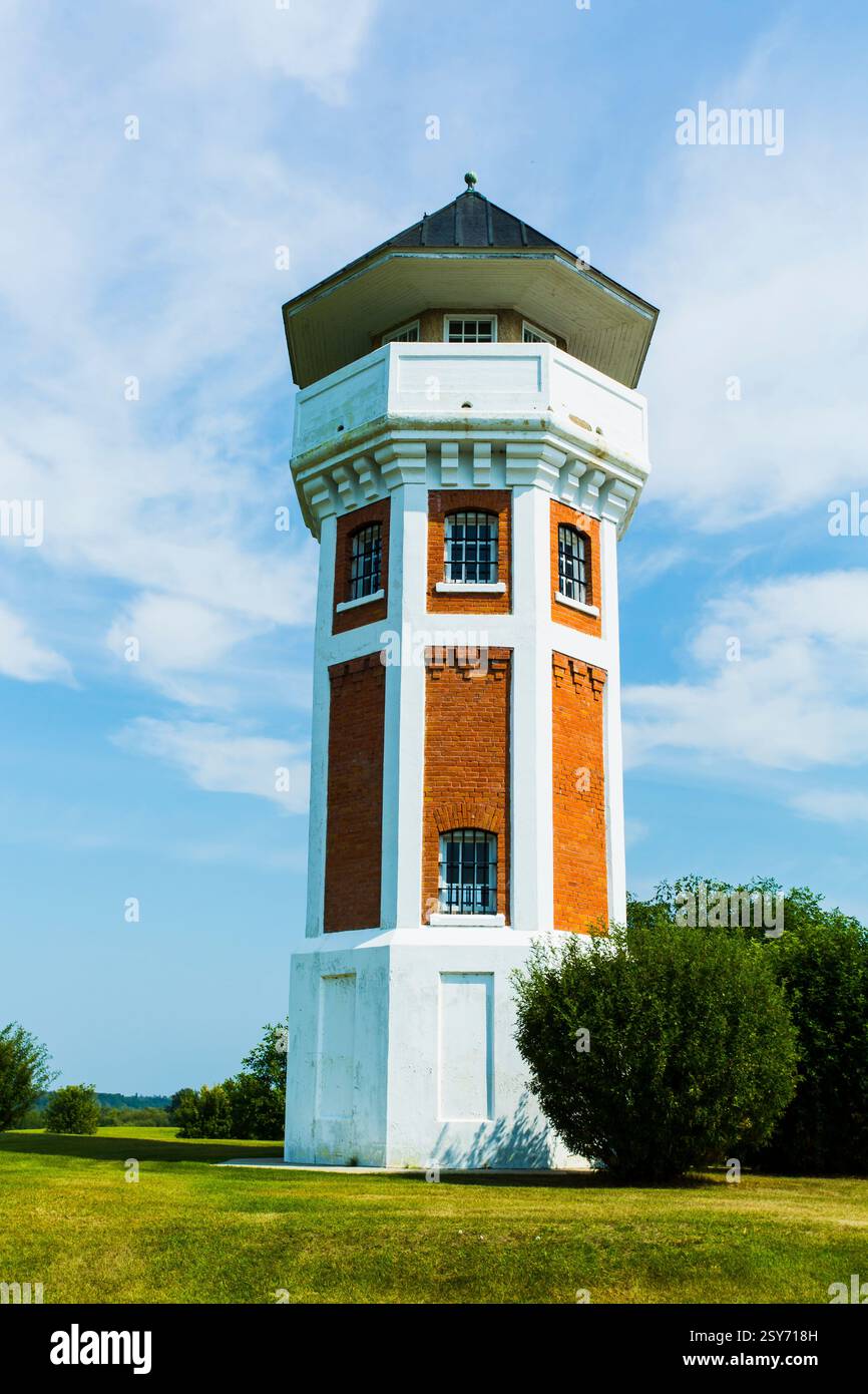 Haute tour de briques avec un toit blanc. La tour est entourée d'herbe. L'herbe est verte et le ciel bleu Banque D'Images