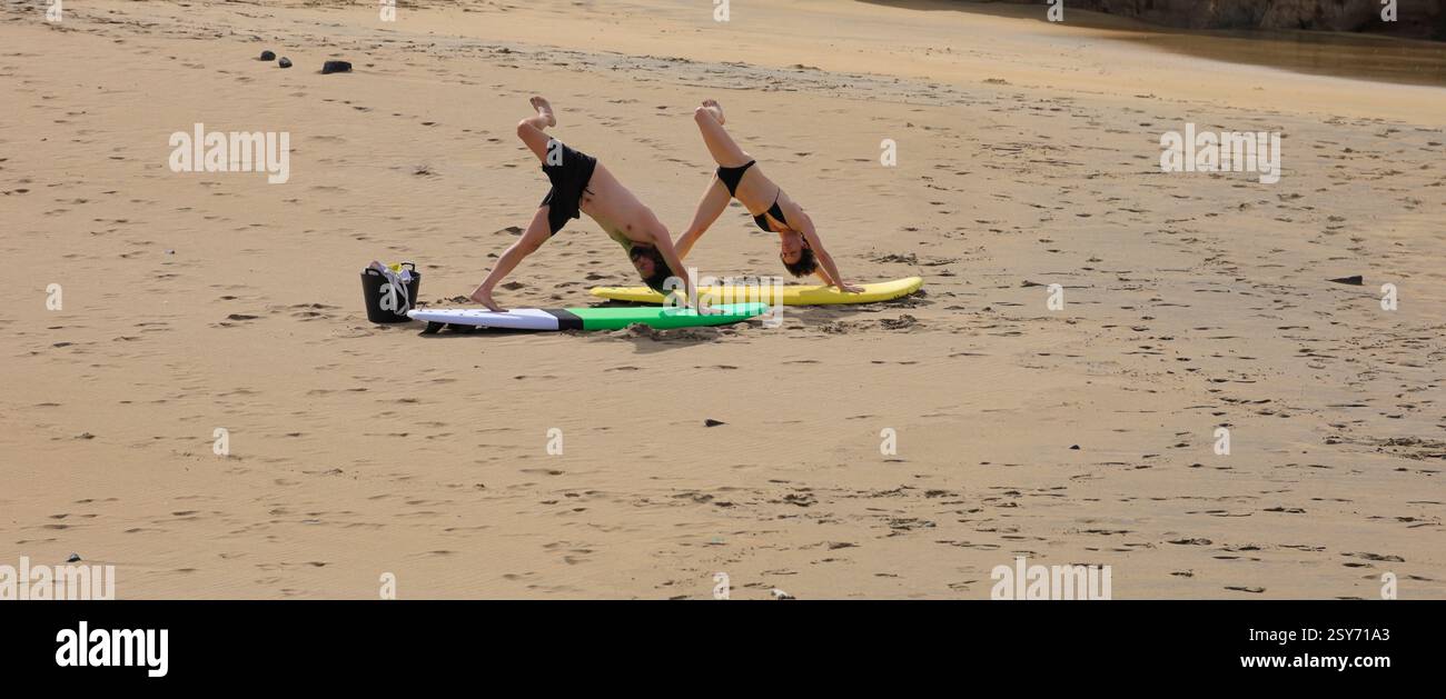 Séance de yoga en plein air, deux personnes pratiquent sur des planches de surf sur une plage, Piedra Playa, Fuerteventura, Îles Canaries, Espagne. Prise 2024 Banque D'Images