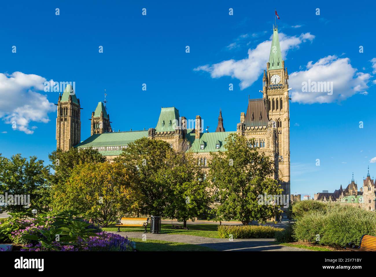 Grand bâtiment avec une tour de l'horloge et un toit vert. Le bâtiment est entouré d'arbres et d'un banc Banque D'Images