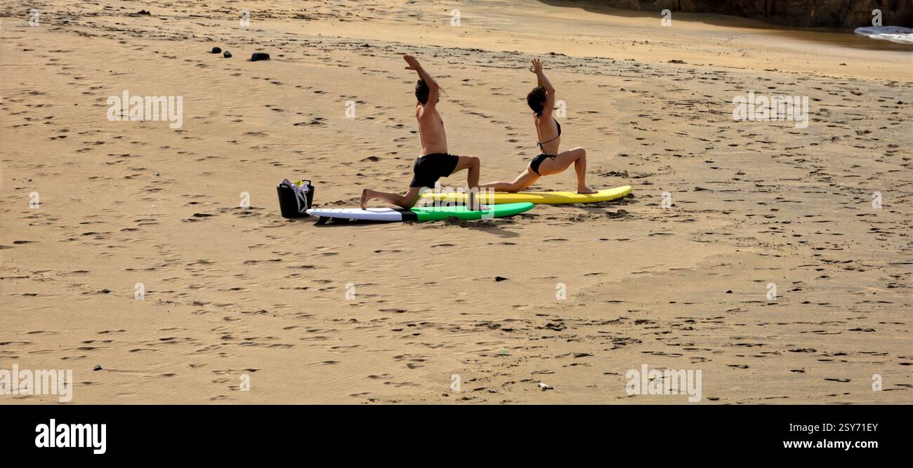 Séance de yoga en plein air, deux personnes pratiquent sur des planches de surf sur une plage, Piedra Playa, Fuerteventura, Îles Canaries, Espagne. Prise 2024 Banque D'Images