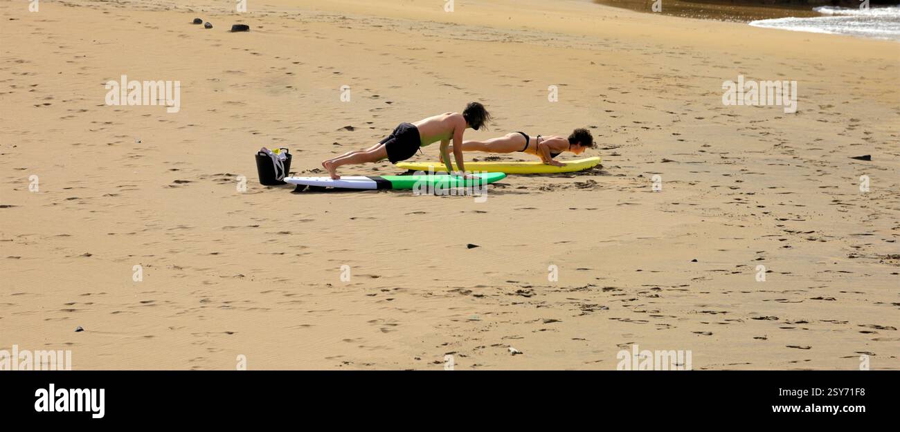 Séance de yoga en plein air, deux personnes pratiquent sur des planches de surf sur une plage, Piedra Playa, Fuerteventura, Îles Canaries, Espagne. Prise 2024 Banque D'Images