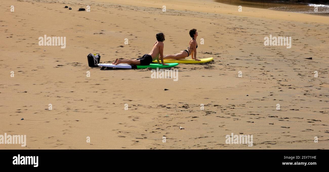 Séance de yoga en plein air, deux personnes pratiquent sur des planches de surf sur une plage, Piedra Playa, Fuerteventura, Îles Canaries, Espagne. Prise 2024 Banque D'Images