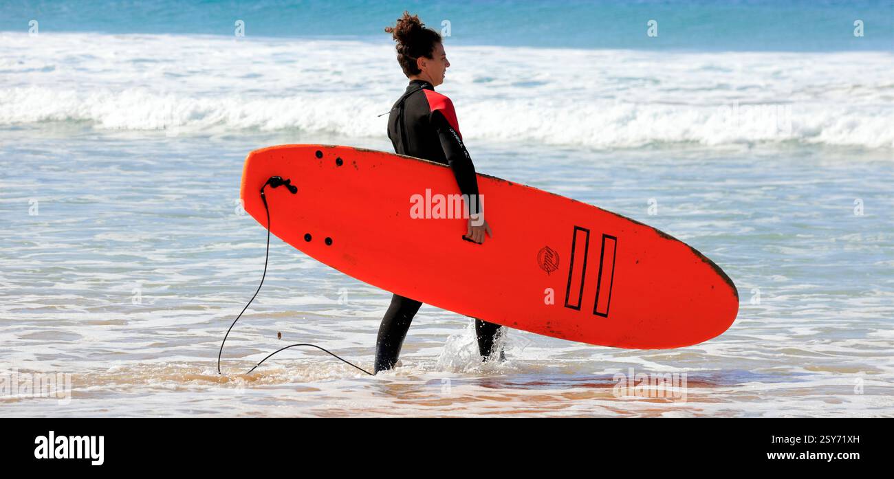 Femme avec planche de surf marchant vers la mer, Fuerteventura, Îles Canaries, Espagne. Prise 2024 Banque D'Images
