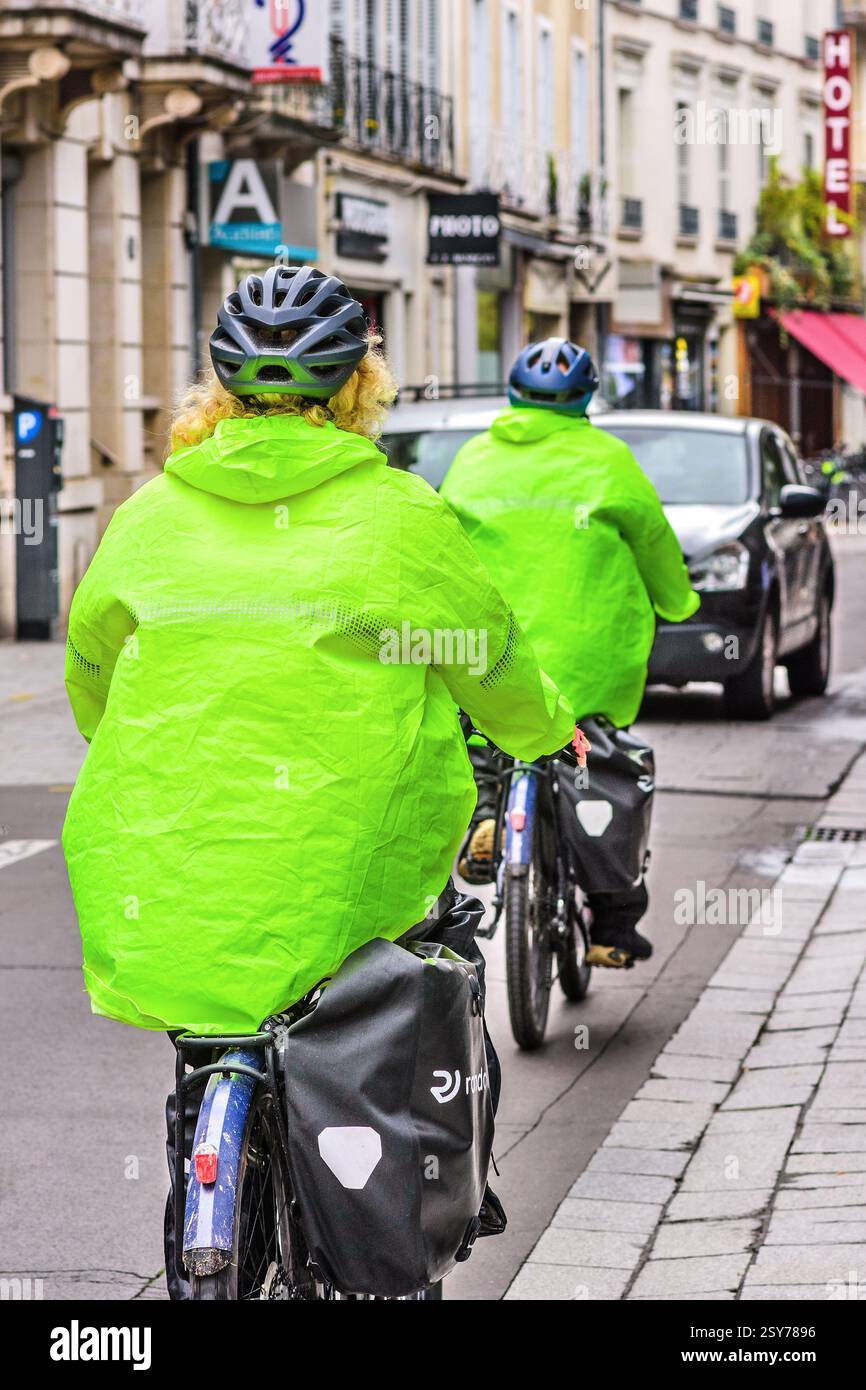Couple en vert vif couleur de sécurité RA-Wear cyclisme le long de la rue du centre-ville - Tours, Indre-et-Loire (37), France. Banque D'Images