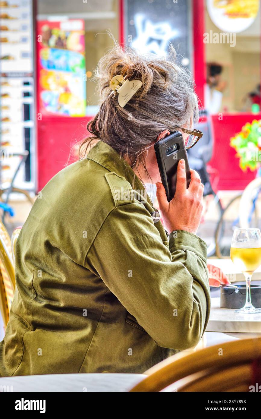 Femme mature assise à la table de café faisant appel sur smartphone - Tours, Indre-et-Loire (37), France. Banque D'Images