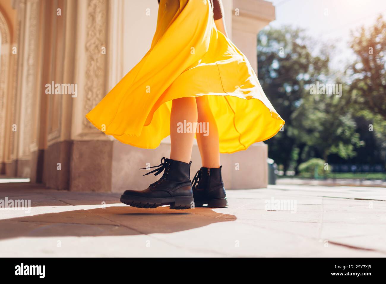 Femme portant une tenue jupe jaune et bottes en cuir noir sur la rue de la ville. Gros plan sur les chaussures et le tissu fluide en mouvement. Vêtements féminins. Banque D'Images