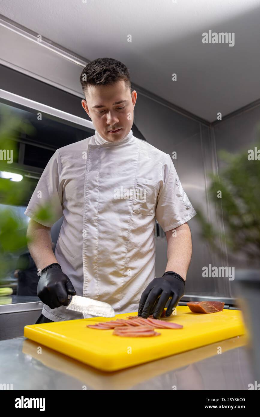 Chef professionnel montrant une tranche parfaite de poisson fumé, démontrant l'expertise culinaire dans une cuisine de restaurant moderne Banque D'Images