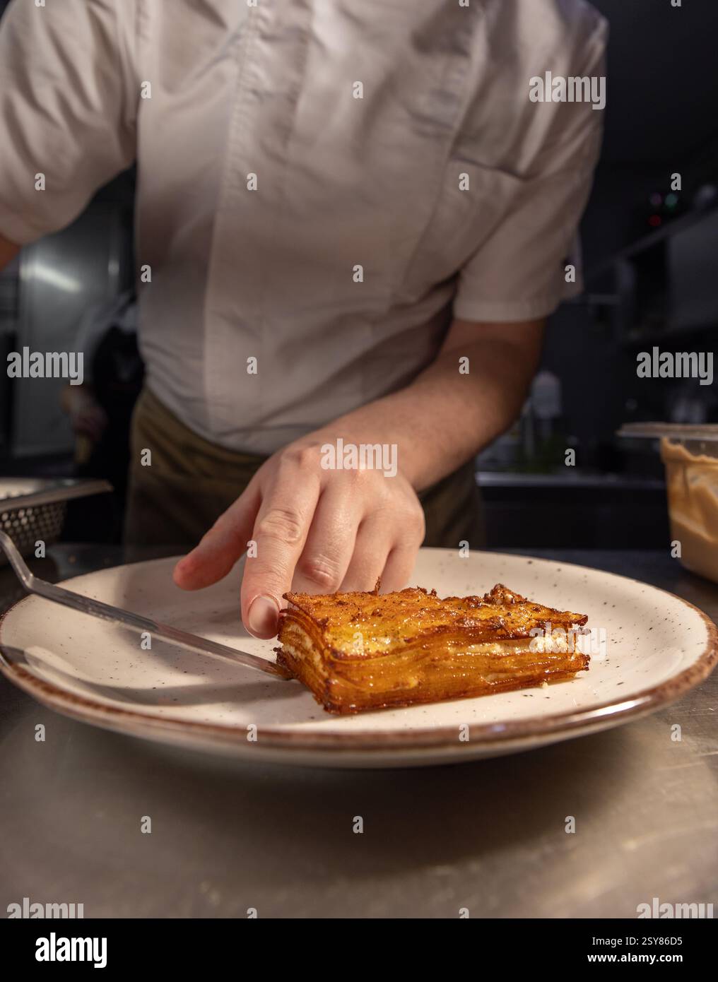 Chef professionnel préparant un délicieux gratin de pommes de terre, mettant en valeur l'expertise culinaire dans un cadre de restaurant Banque D'Images
