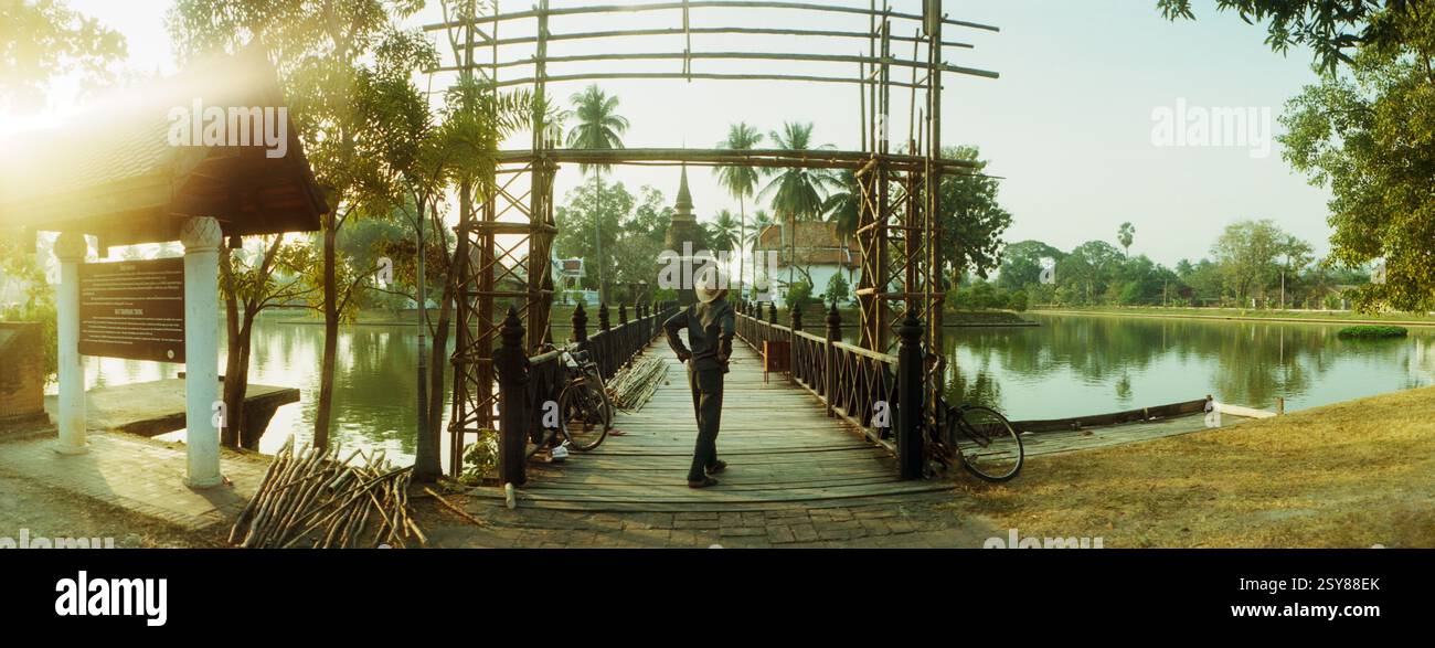 Vue panoramique de l'homme reconstruisant l'entrée d'un pont en bois menant à un temple bouddhiste, parc historique de Sukhothai, Sukhothai, Thaïlande Banque D'Images