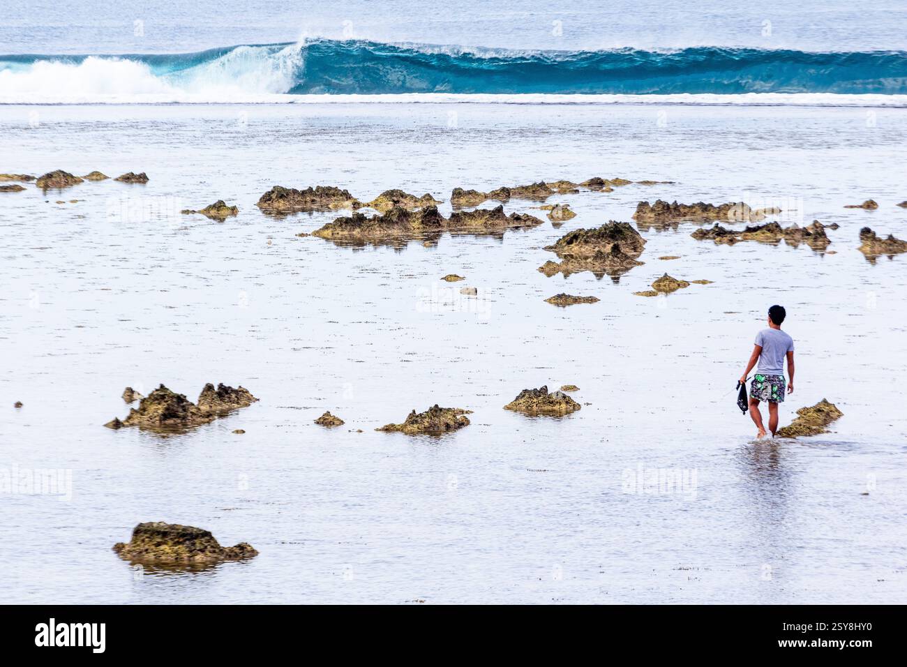 Homme pataugant dans l'eau peu profonde près d'une plage rocheuse sur l'île de Siargao Philippines Banque D'Images