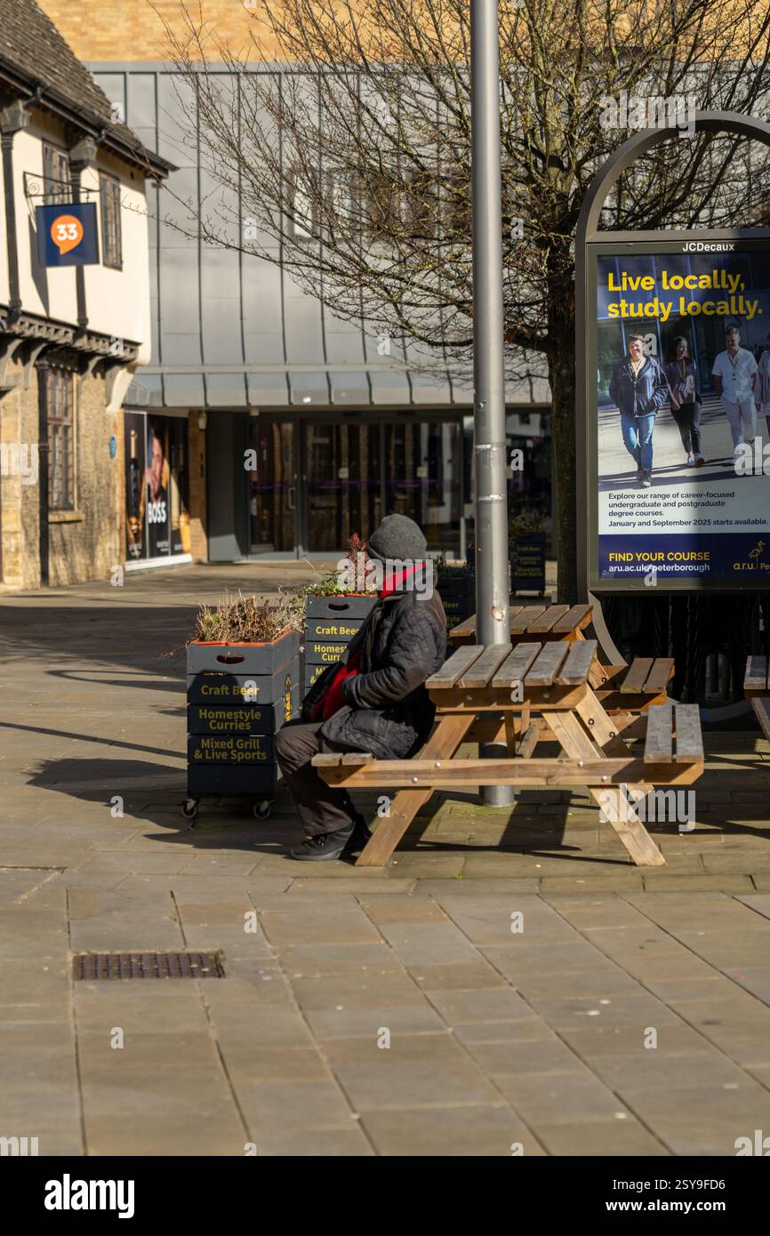 Homme solitaire assis à une table de pique-nique dans un centre-ville déserte, emballé dans des vêtements d'hiver, profitant du calme et des environs Banque D'Images