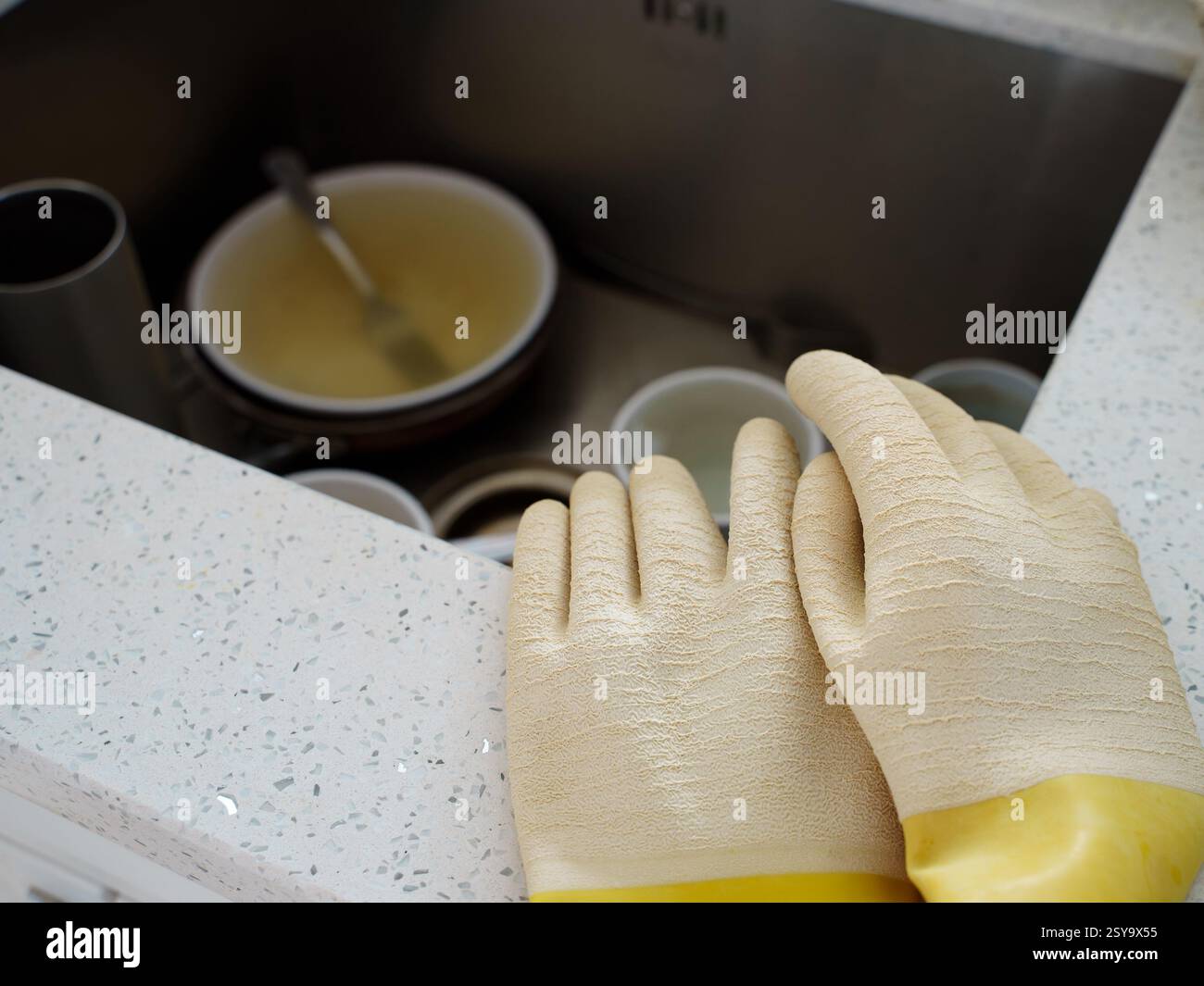 Gants en caoutchouc jaune et beige sur le comptoir de cuisine au-dessus de la vaisselle sale dans l'évier Banque D'Images