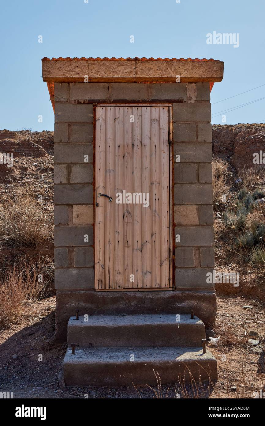 Toilettes extérieures à la campagne. Cabine de toilettes à blocs de béton avec porte en bois. Banque D'Images