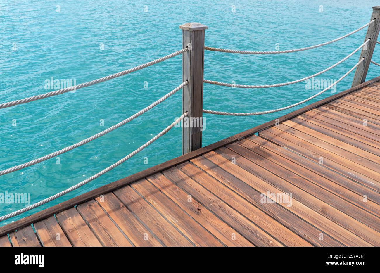 Jetée en bois avec poteaux et cordes avec de l'eau de mer scintillante. Jetée en bois avec fond bleu de mer. Banque D'Images
