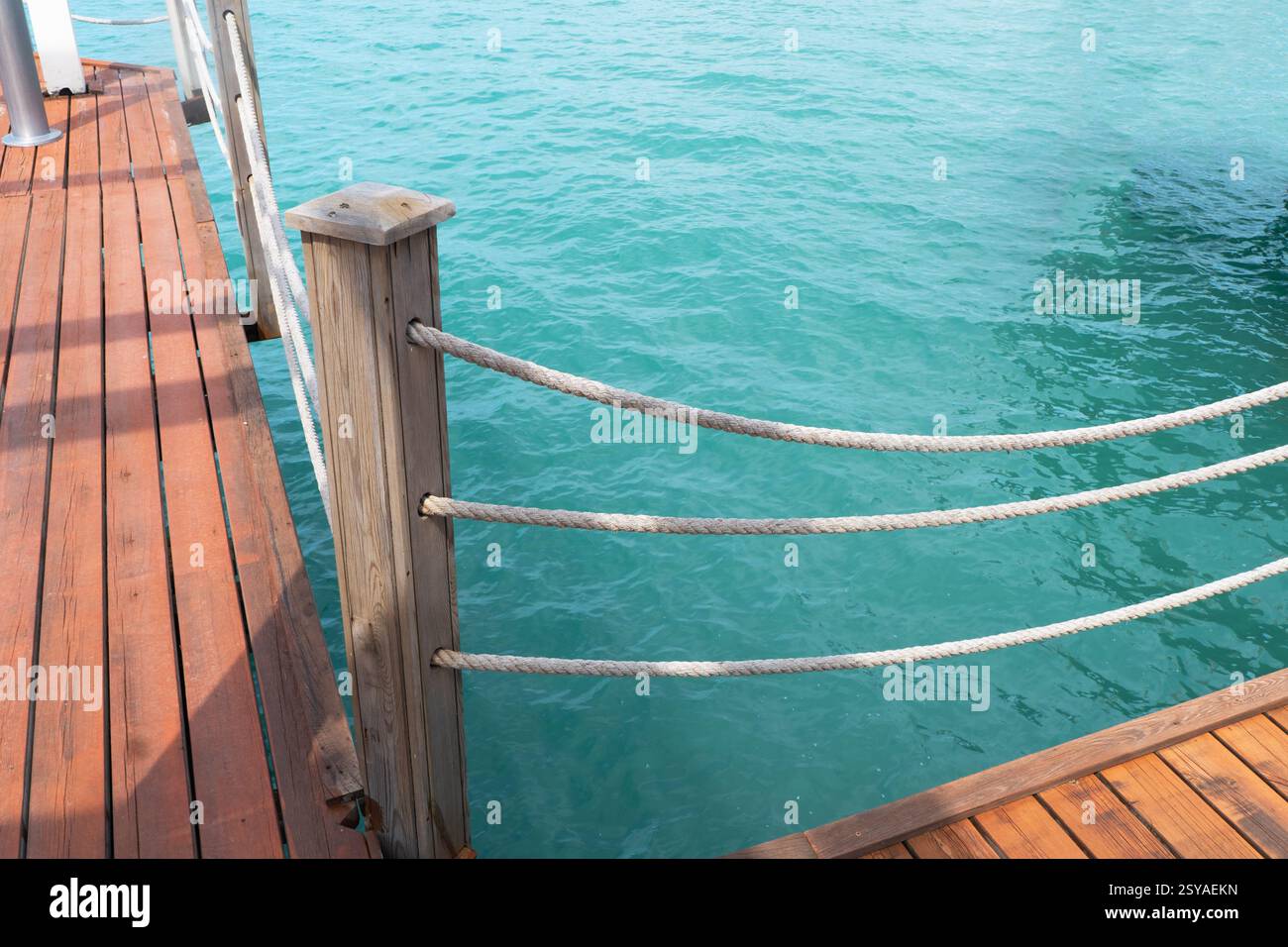 Jetée en bois avec poteaux et cordes avec de l'eau de mer scintillante. Jetée en bois avec fond bleu de mer. Banque D'Images