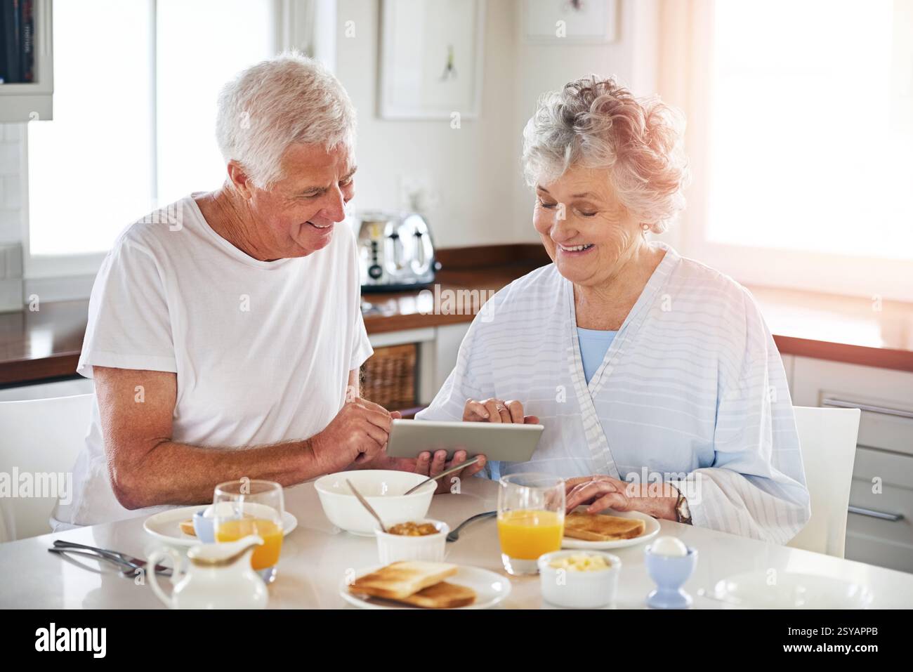 Sourire, couple senior et tablette dans la cuisine sur les médias sociaux, lire blog et recherche sur Internet. Personnes âgées, application numérique et liaison pour le petit déjeuner Banque D'Images