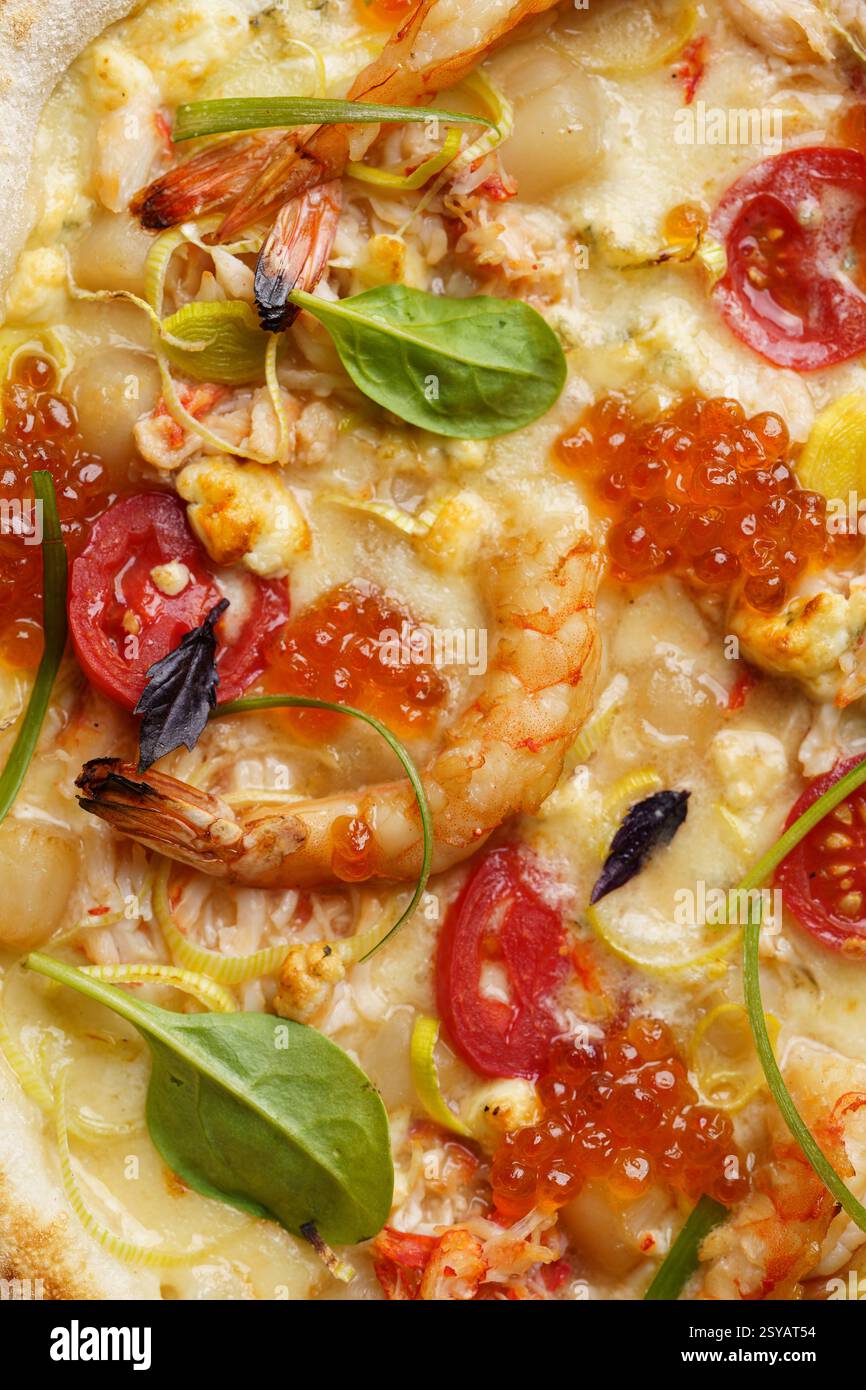 Vue rapprochée d'une délicieuse pizza gastronomique garnie de crevettes succulentes, de caviar rouge vif, de mozzarella crémeuse, de tomates tranchées, d'épinards au basilic, et s. Banque D'Images