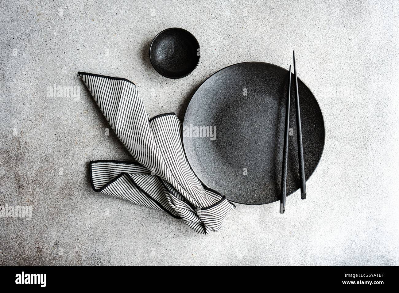 Une table minimaliste en noir et blanc avec une assiette noire, une serviette rayée et des baguettes crée une expérience culinaire sophistiquée. Parfait pour e. Banque D'Images