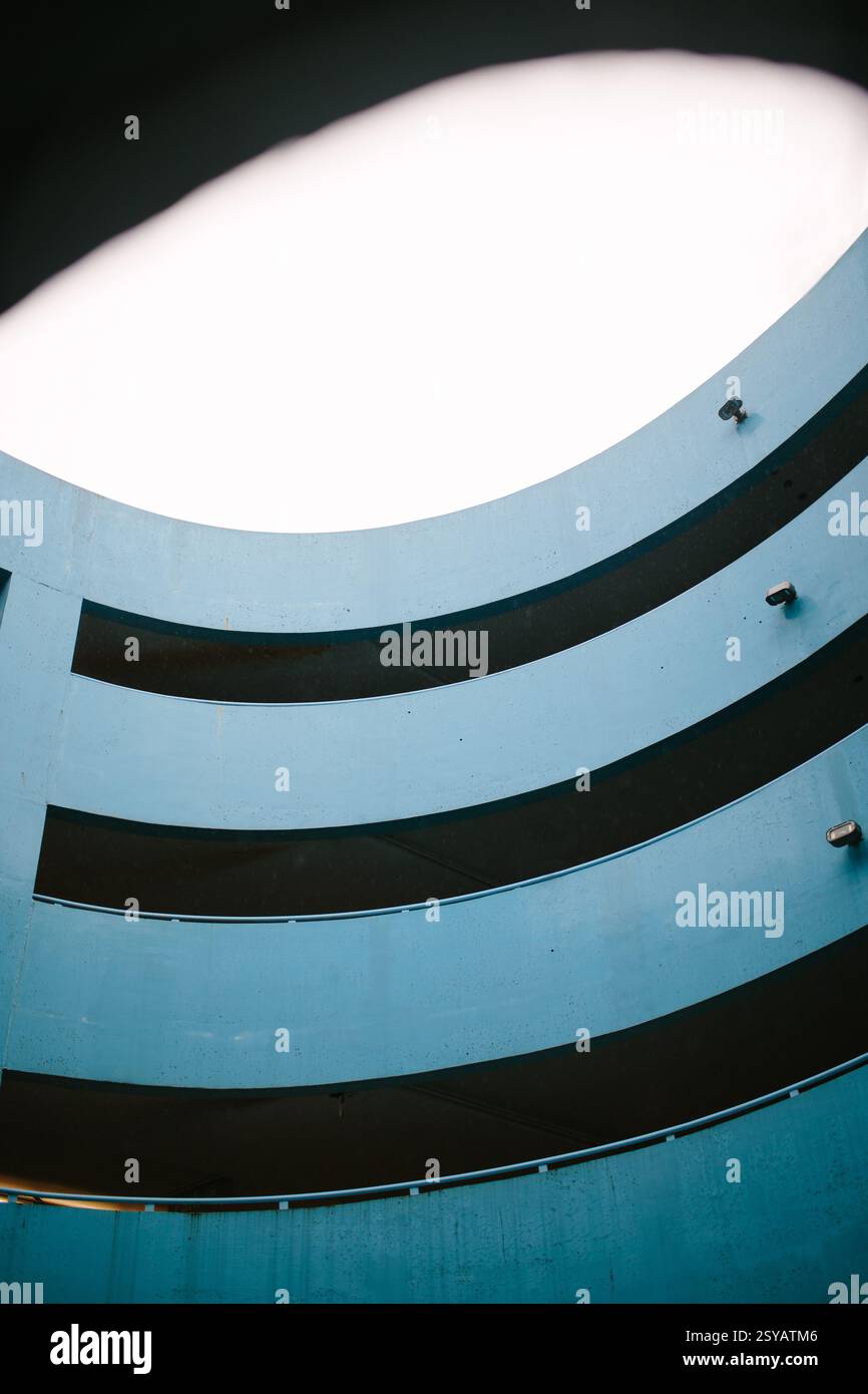Un parking bleu moderne doté d'un design circulaire à plusieurs niveaux amélioré par un éclairage doux à partir d'une ouverture au plafond. L'accent sur les détails architecturaux Banque D'Images