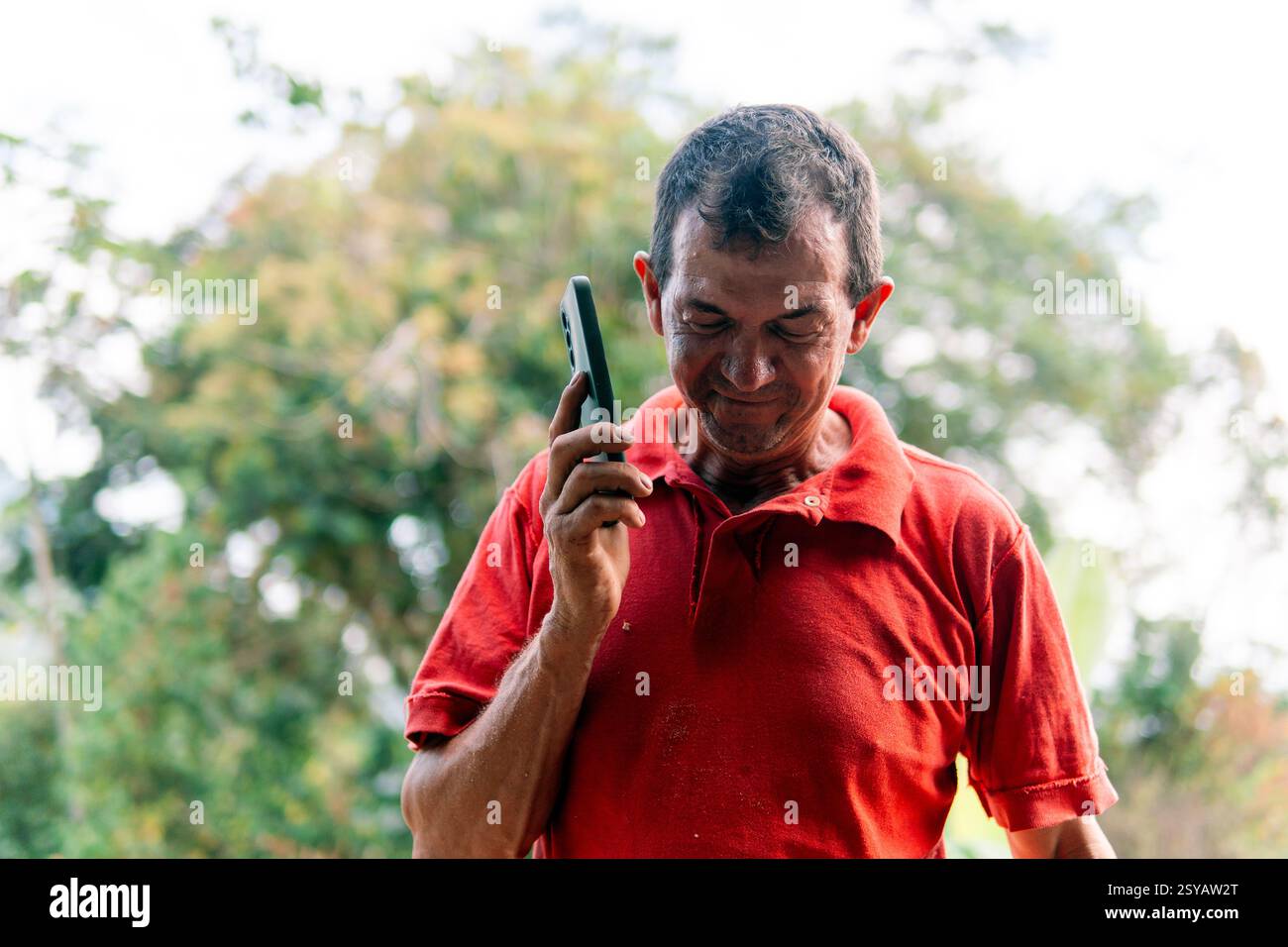Agriculteur méconnaissable utilisant un smartphone pendant une pause, au milieu du travail manuel dans la campagne colombienne luxuriante, représentant un mélange de traditionnel Banque D'Images