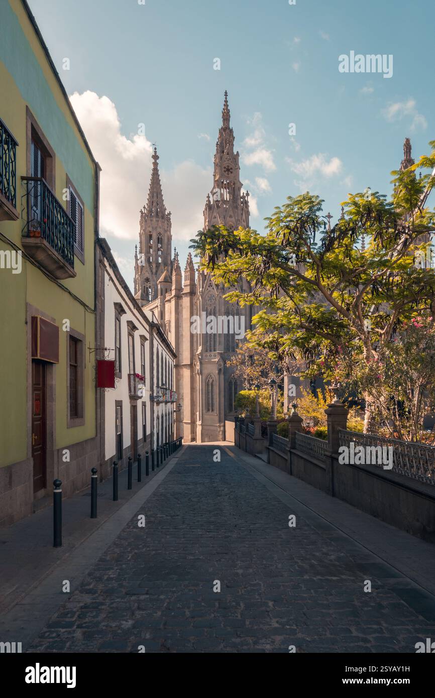 Une vue pittoresque d'une rue pavée à Arucas, menant directement aux flèches imposantes de l'église San Juan Bautista sous un ciel serein, Banque D'Images