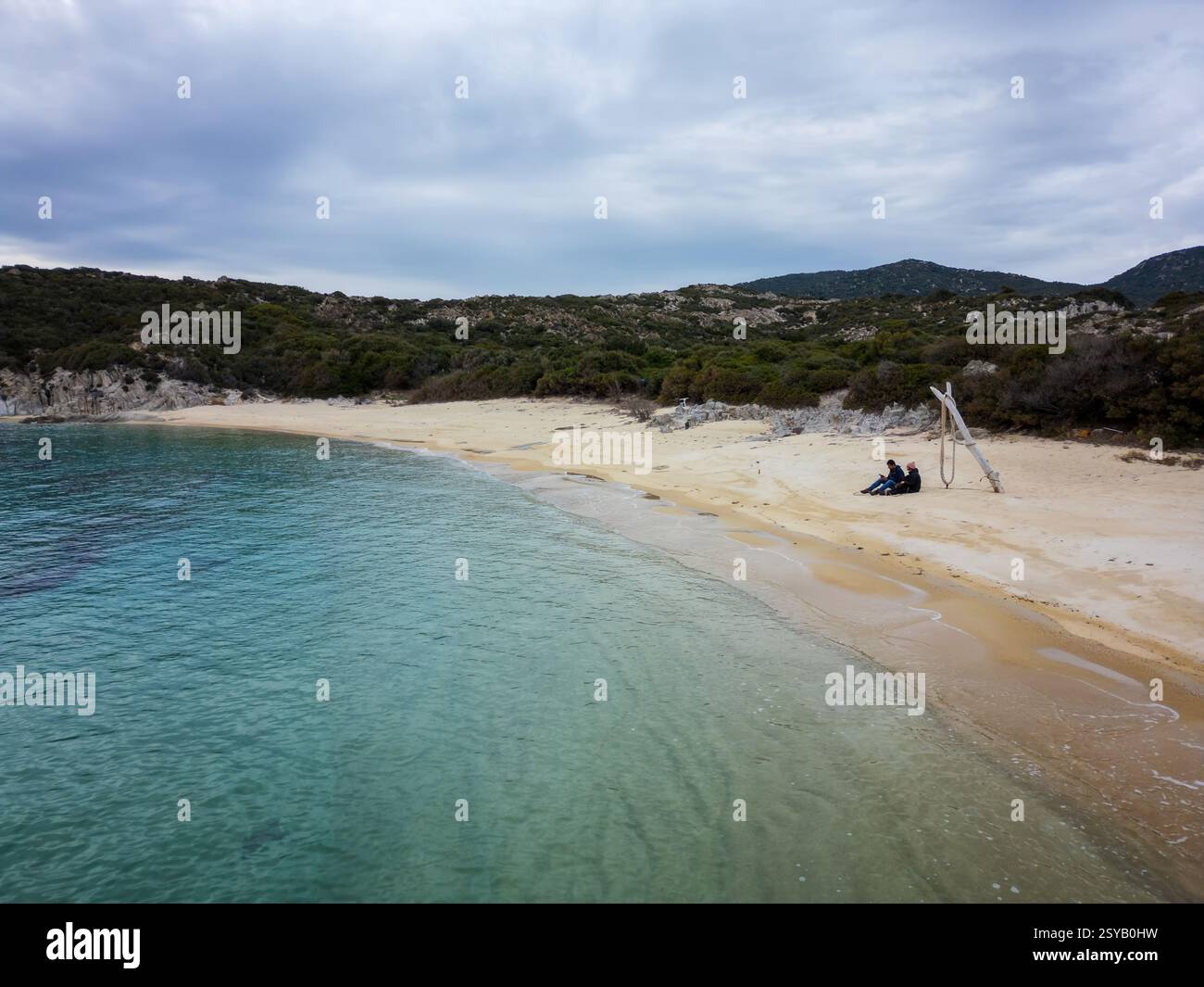 Une vue aérienne paisible de la plage sauvage de Kalamitsi en Grèce. Un couple est assis sur le sable doré au bord des eaux turquoises, entouré d'une verdure luxuriante et d'une sere Banque D'Images