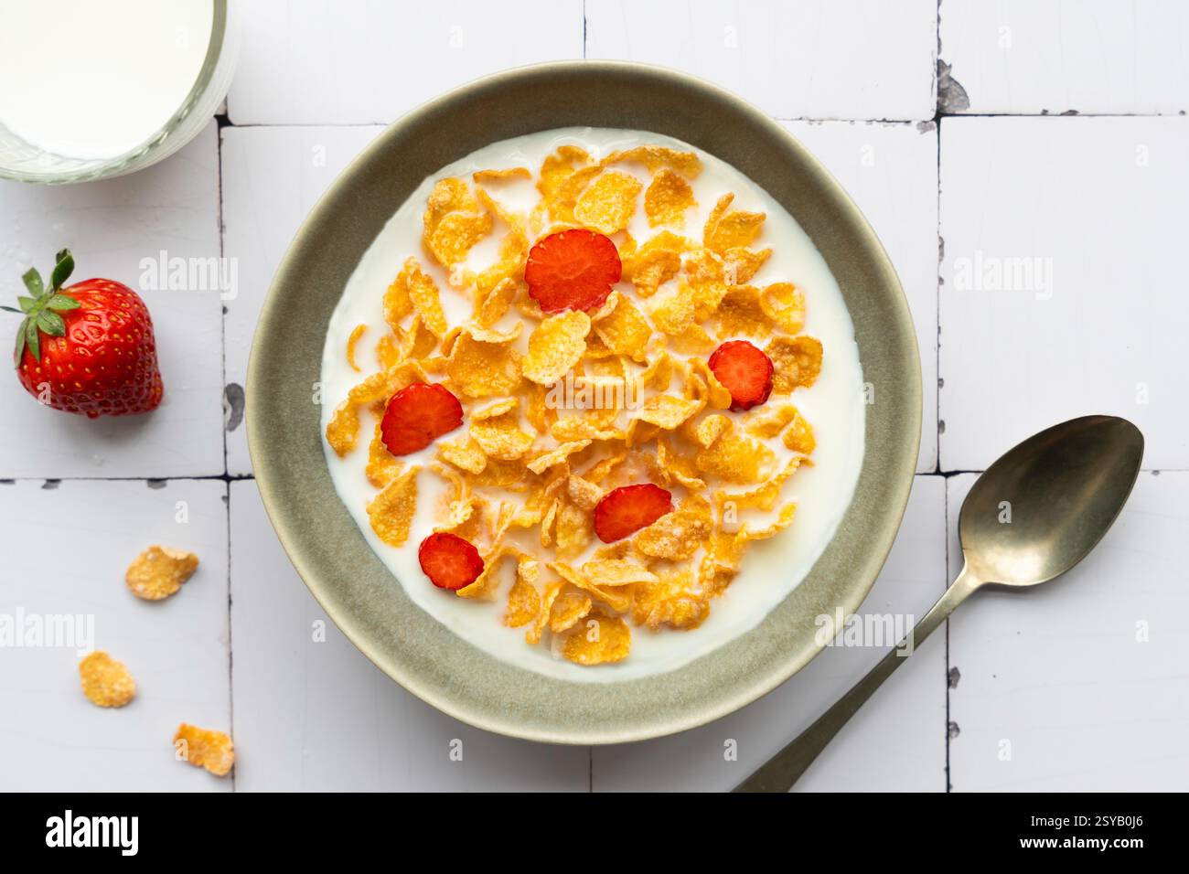 Un bol de cornflakes croquants avec des tranches de fraises fraîches, servi dans du lait. Un petit déjeuner sain avec un verre de lait et une cuillère placée près de Banque D'Images
