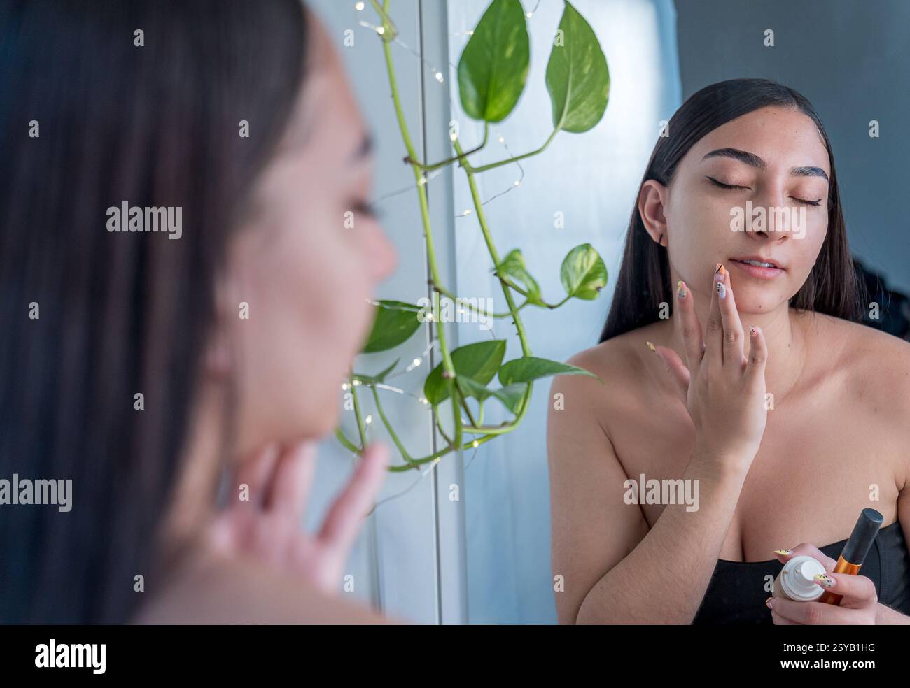 Une femme applique de la crème de soin sur son visage devant un miroir. Elle se concentre sur les soins personnels, avec une atmosphère relaxante et un éclairage naturel enhancin Banque D'Images