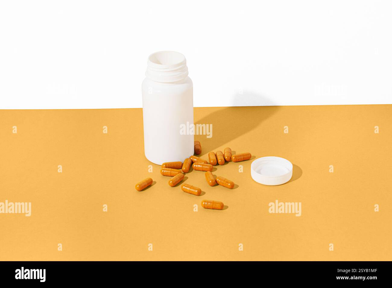 Une bouteille blanche avec son couvercle retiré repose sur une surface jaune, entourée de capsules orange dispersées. La configuration lumineuse et minimaliste souligne les contras Banque D'Images
