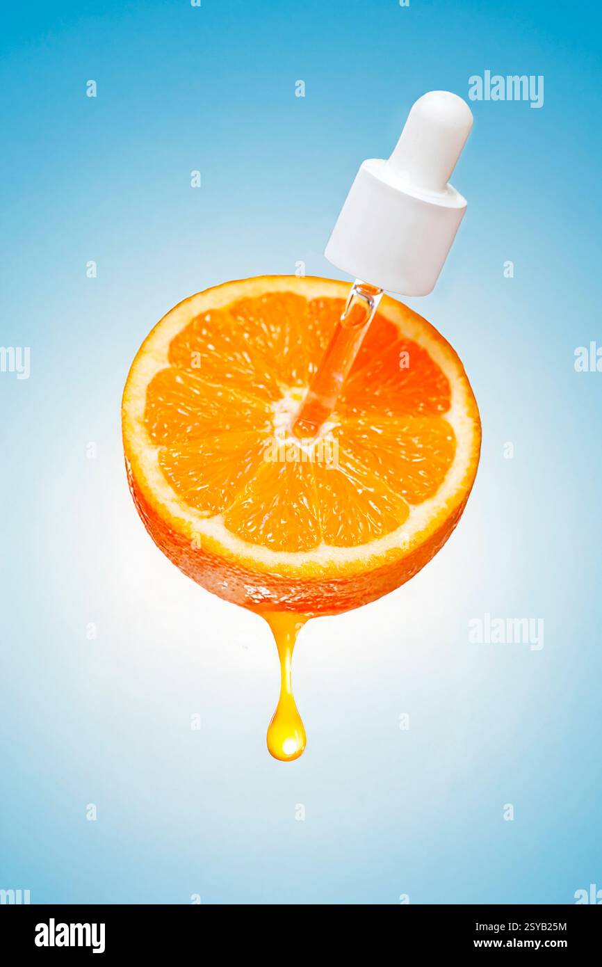 Un compte-gouttes libère un liquide clair sur une tranche fraîche d'orange, avec une goutte de jus qui coule sur un fond bleu. Banque D'Images