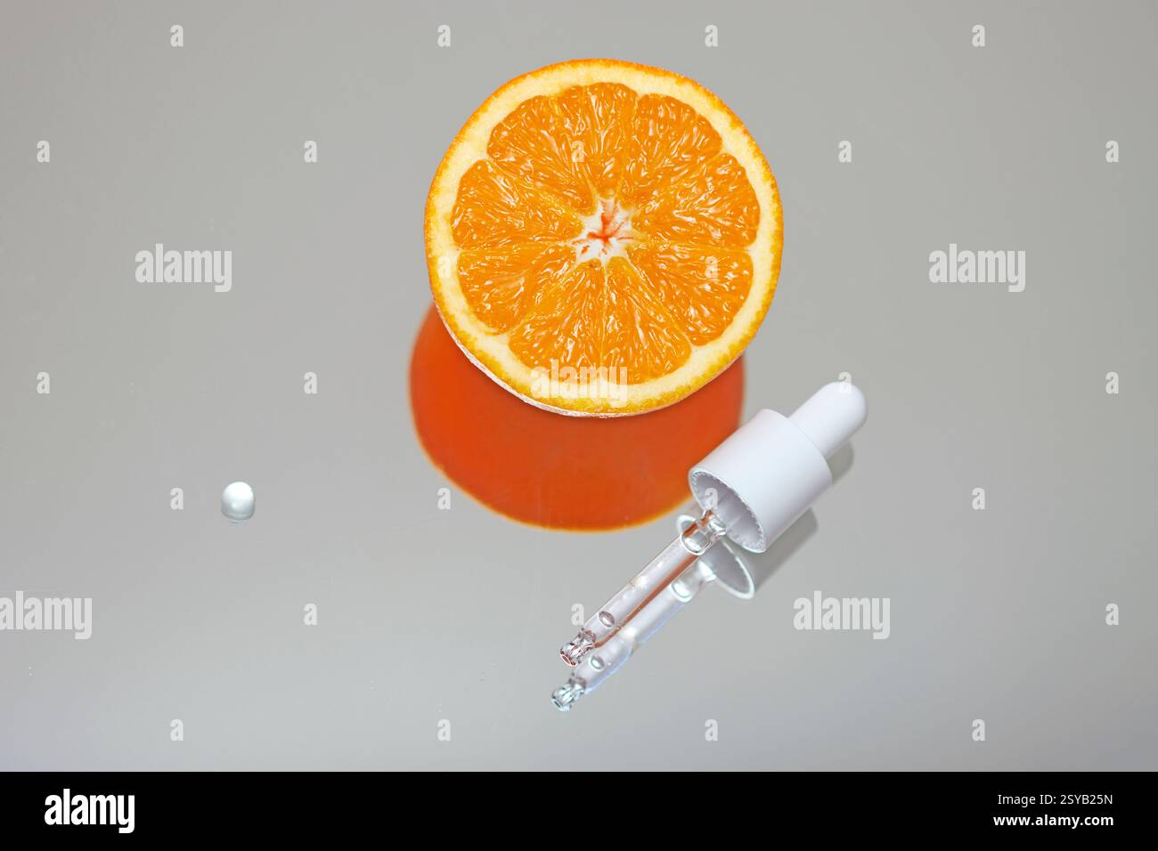 Une moitié orange fraîche à côté d'un compte-gouttes en verre sur une surface réfléchissante, suggérant un concept d'extraction d'essence naturelle ou de supplémentation en vitamine C. Banque D'Images